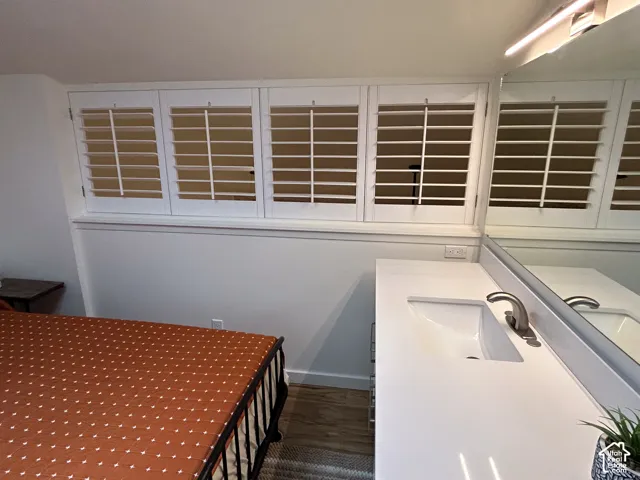 White plantation shutters, integrated vanity with single basin sink, wall-mounted mirror, and wood-finish flooring