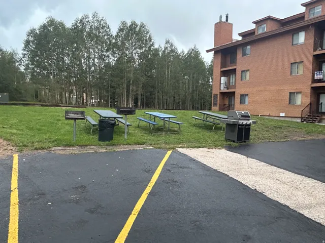 Outdoor communal area with paved parking, a grassy expanse, and mature trees