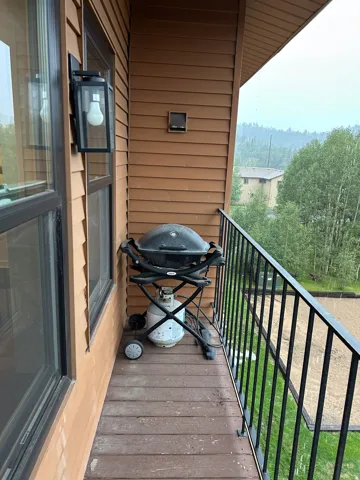 Balcony with wood-finish decking, black metal railing, and wall-mounted exterior lighting