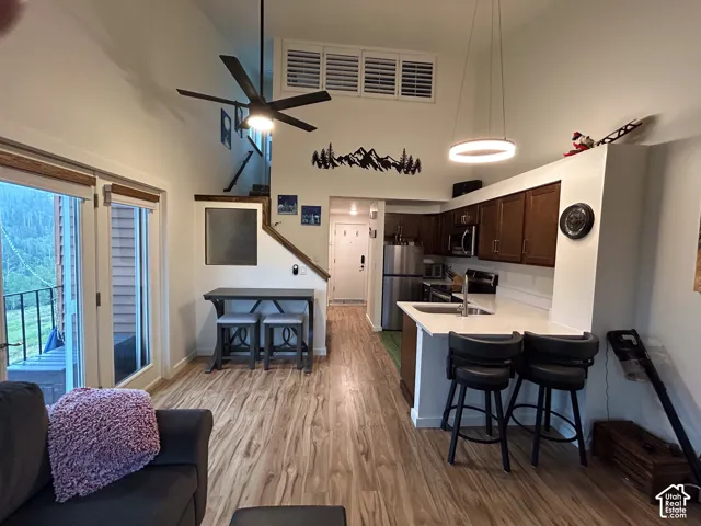 Vaulted ceiling with a ceiling fan, wood-finish flooring, kitchen with stainless steel appliances, white countertops, and wood cabinetry, and a glass-paneled door