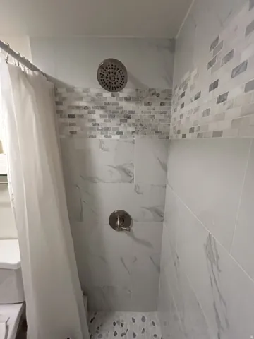 Shower with large format wall tiles, a decorative mosaic tile band, pebble-finish flooring, and a brushed nickel showerhead