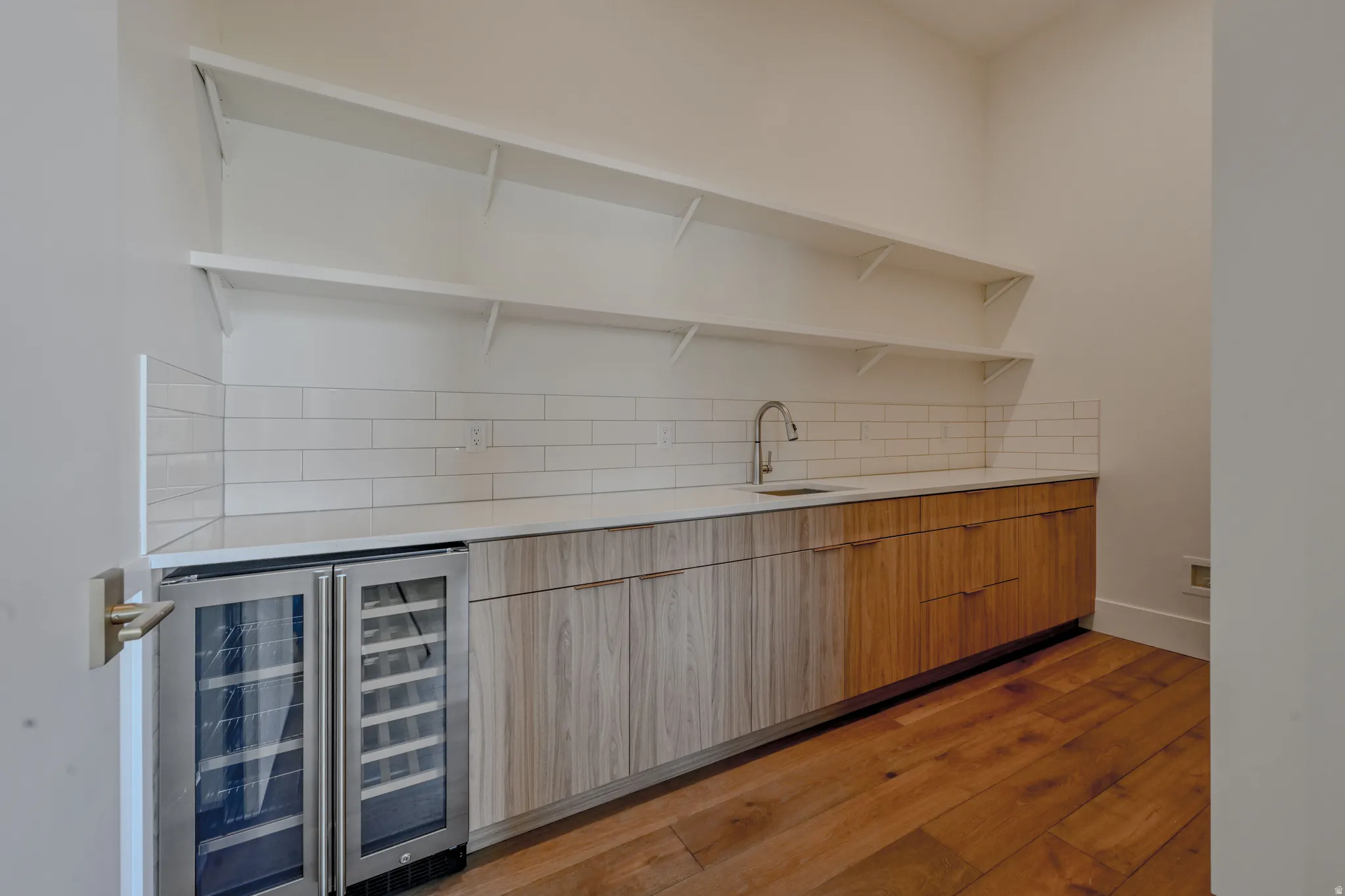 Built-in cabinetry with a light-toned countertop, stainless steel beverage refrigerators, and a subway tile backsplash
