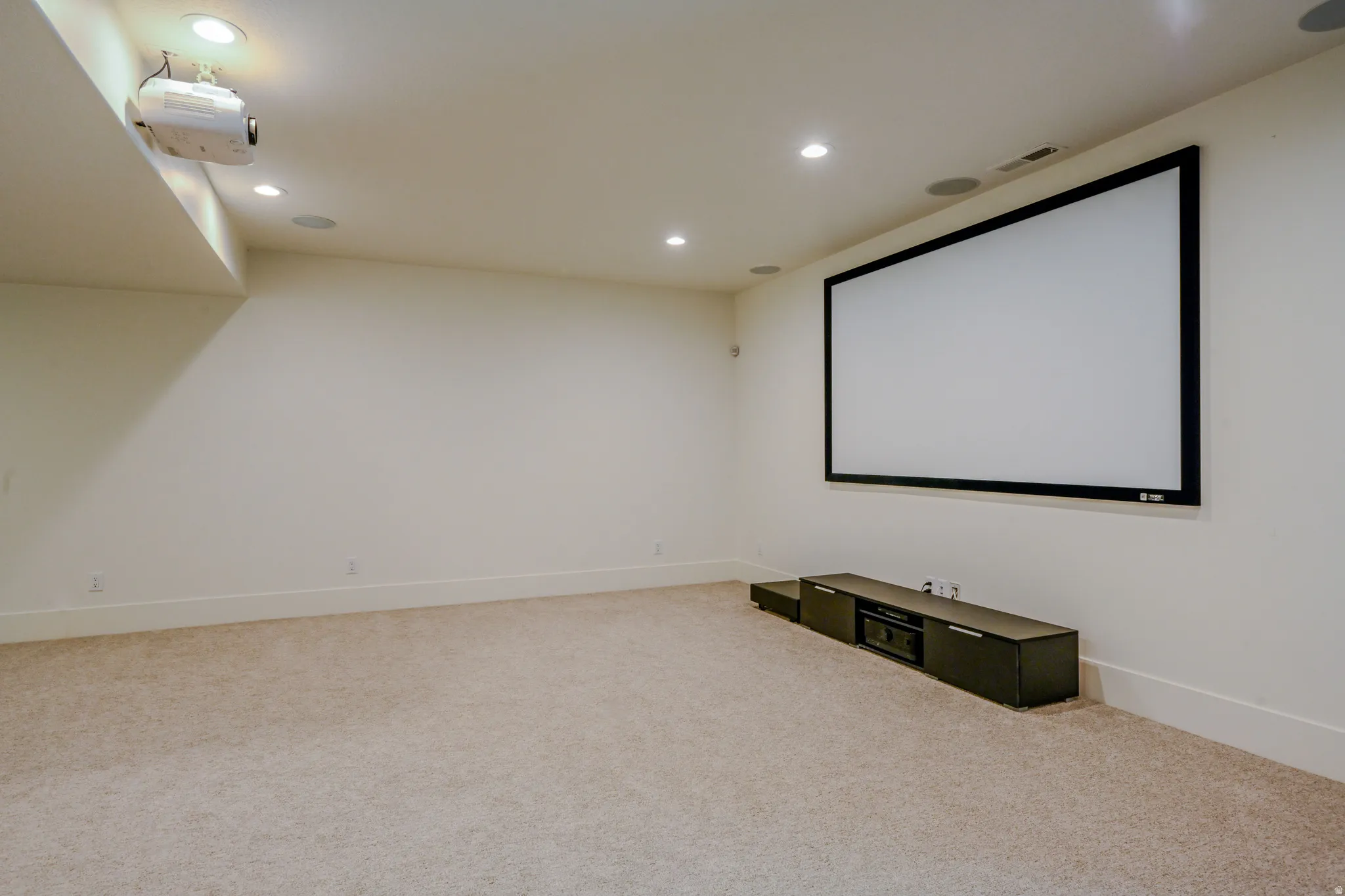 Built-in projector with a large fixed screen, recessed lighting, integrated ceiling speakers, and plush carpet flooring