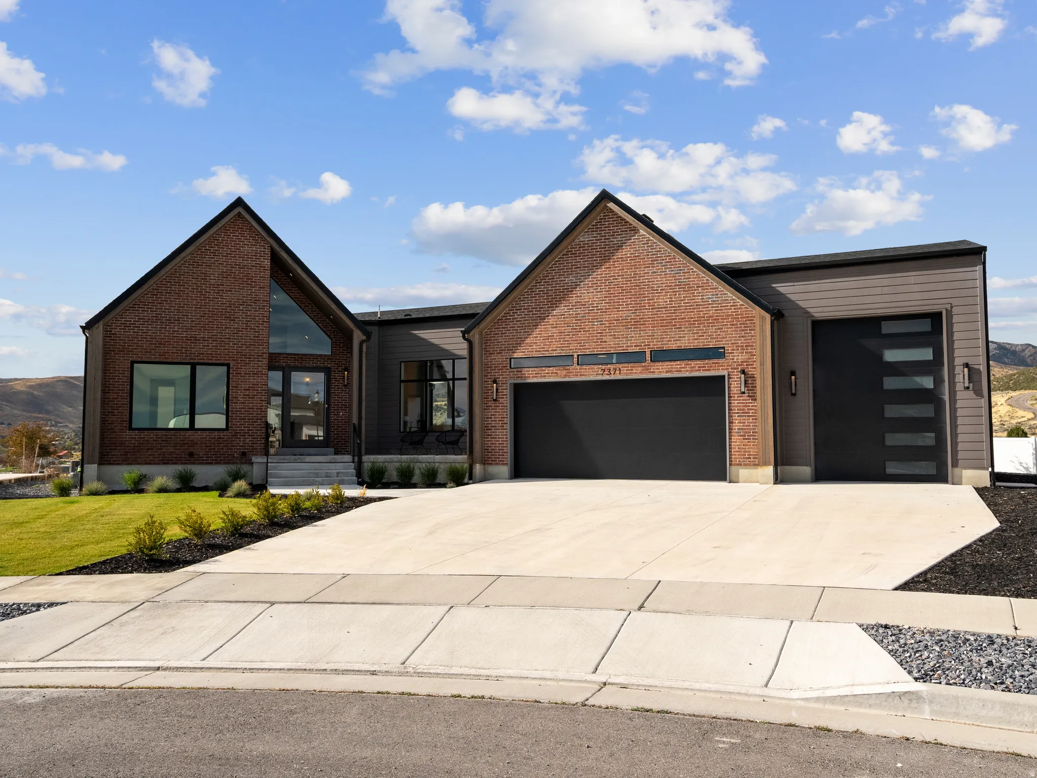 Contemporary exterior featuring brick and horizontal siding, two distinct garage doors, a concrete driveway, and front landscaping