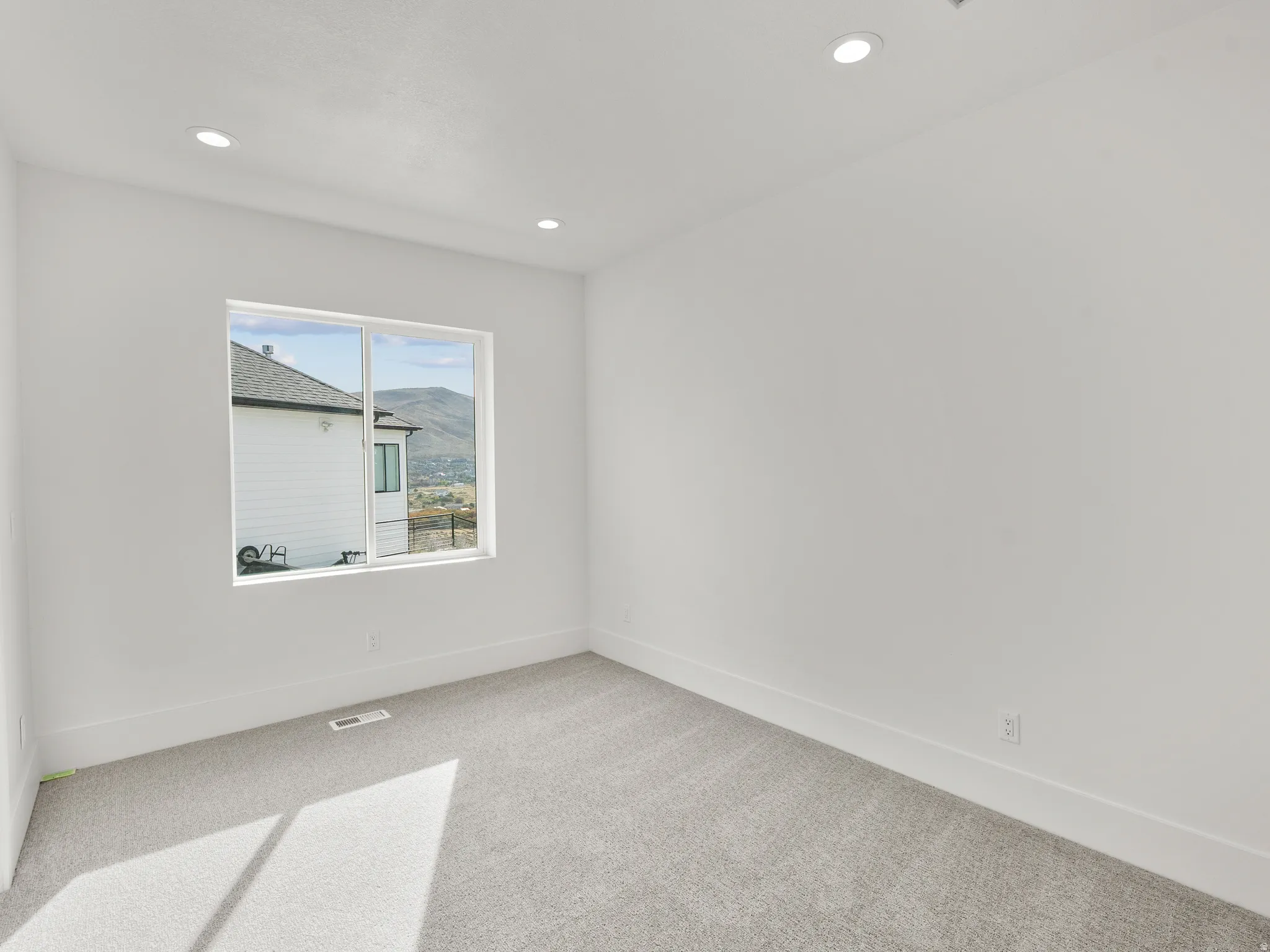 Recessed lighting, light gray carpeting, and white walls with a large window