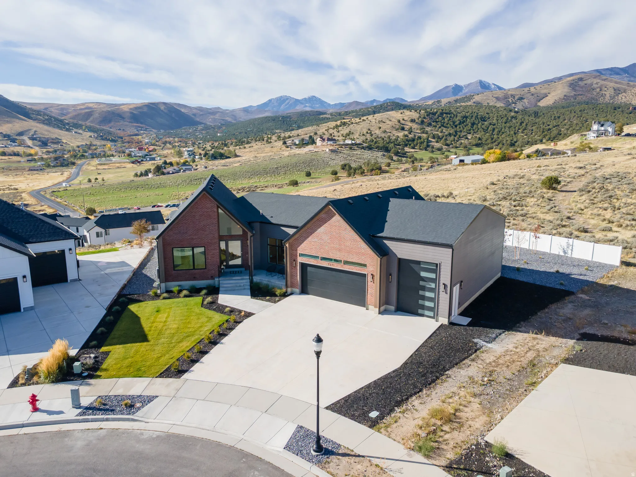 Contemporary architecture featuring a red brick and dark gray siding exterior, peaked rooflines, a concrete driveway, and a landscaped front yard