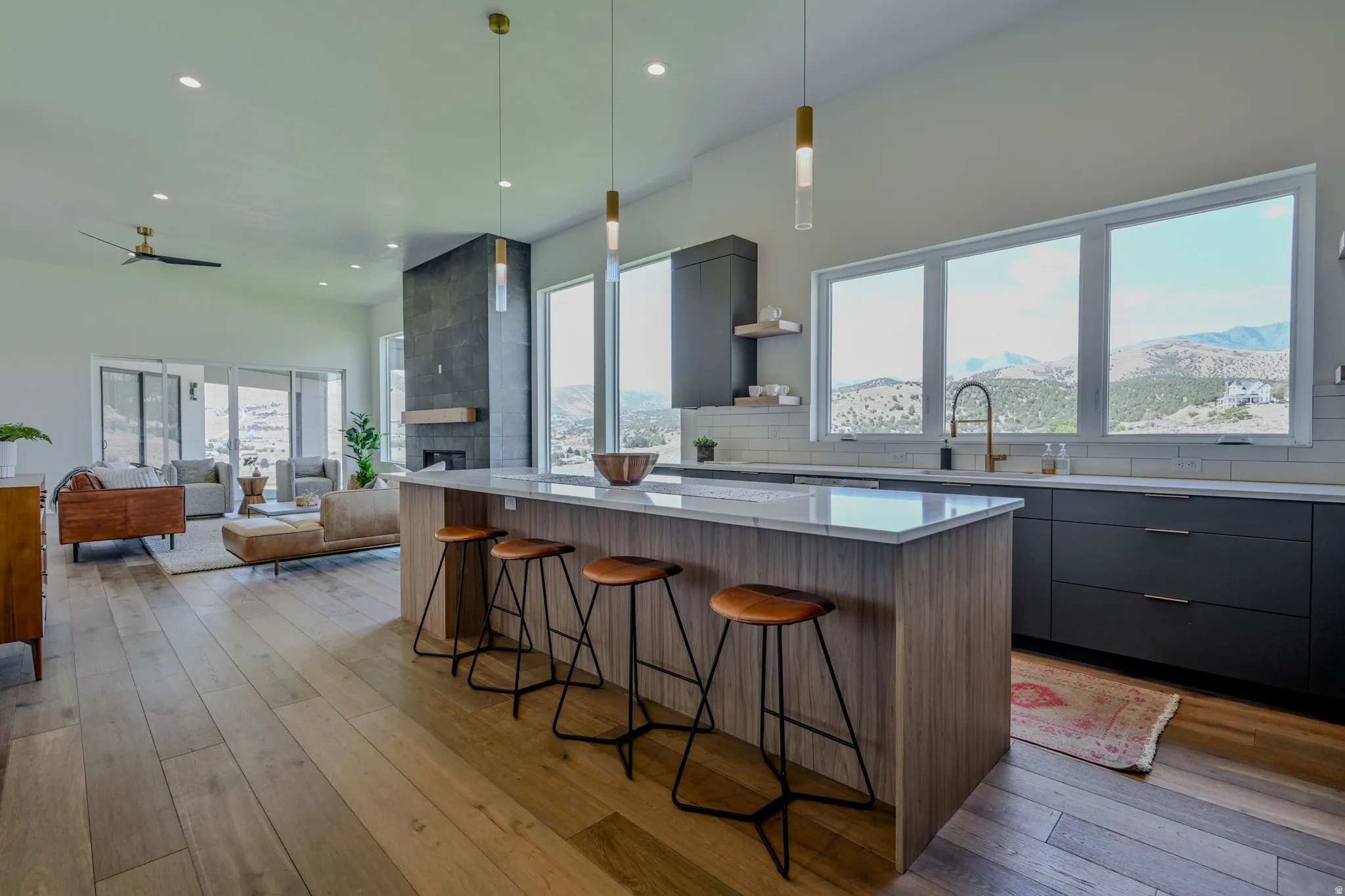 Open-concept design featuring wood-finish flooring, a kitchen island with seating, dark wood-finish cabinetry, and a contemporary fireplace with a floating mantel