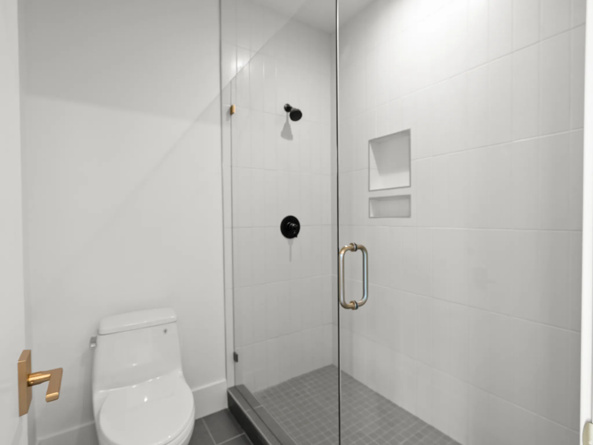 Glass-enclosed shower with white tiled walls, dual recessed shower niches, and matte black fixtures