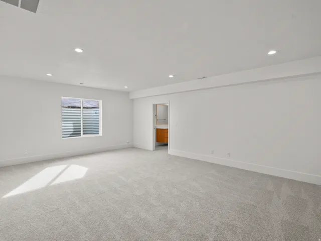 Recessed lighting throughout, light gray carpet flooring, and a large window with a security grate