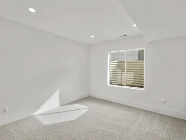 Recessed lighting, light-toned carpeting, white walls, and a window with a window well