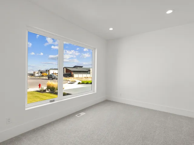 Recessed lighting illuminating a neutrally painted room with a large window and gray carpeting