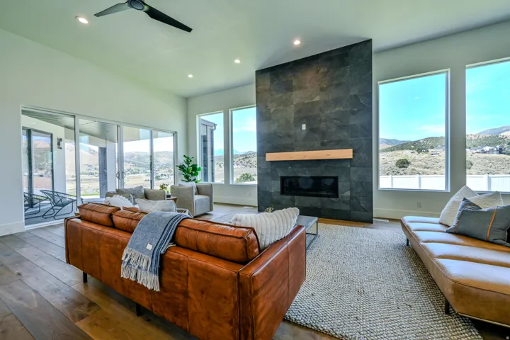 Spacious living area featuring high vaulted ceilings, expansive sliding glass doors, multiple large windows, wood-finish flooring, and a floor-to-ceiling stone-clad fireplace with a wood mantle