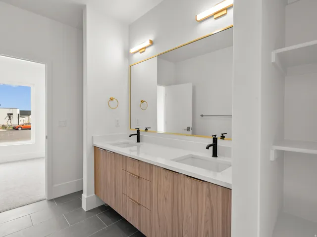 Dual vanity with wood-finish cabinetry and integrated sinks, matte black fixtures, gold-framed mirror, and integrated shelving