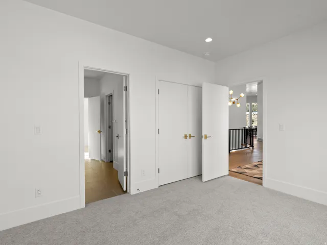 Recessed lighting, light gray carpeting, crisp white walls, and bright white doors with modern gold hardware