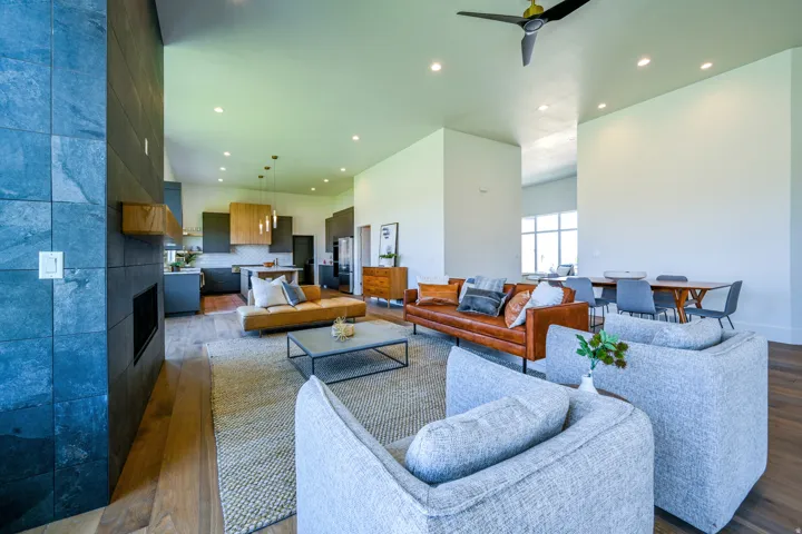 Open-concept living area with high ceilings, wood-finish flooring, a stone-clad fireplace, and recessed lighting