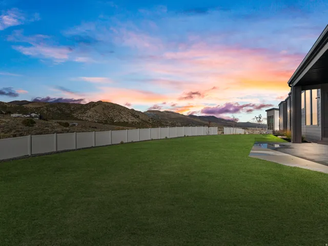 Expansive lawn area, concrete patio, privacy fencing, mountain backdrop, and modern exterior design