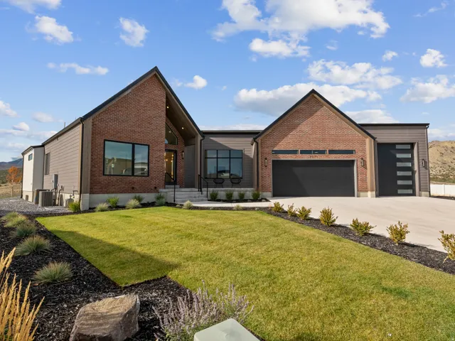 Modern exterior featuring a prominent brick facade, dark-framed windows, an attached two-car garage, an additional single-car garage with frosted glass panels, and a concrete driveway