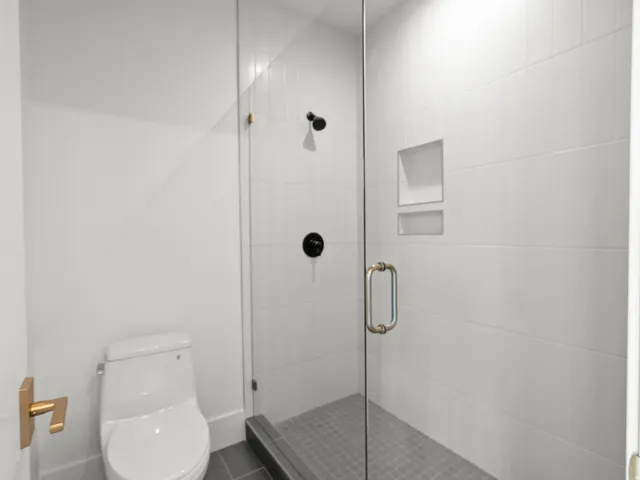 Glass-enclosed shower with white tiled walls, dual recessed shower niches, and matte black fixtures