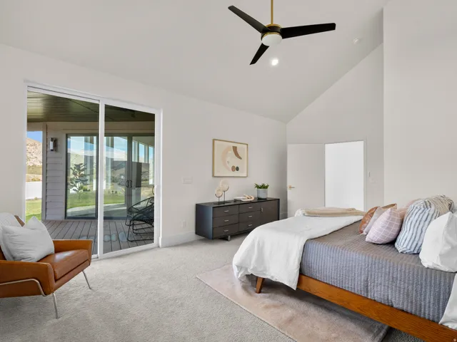 Vaulted ceiling with an integrated ceiling fan, carpeted flooring, sliding glass door to a private deck, and a built-in dresser