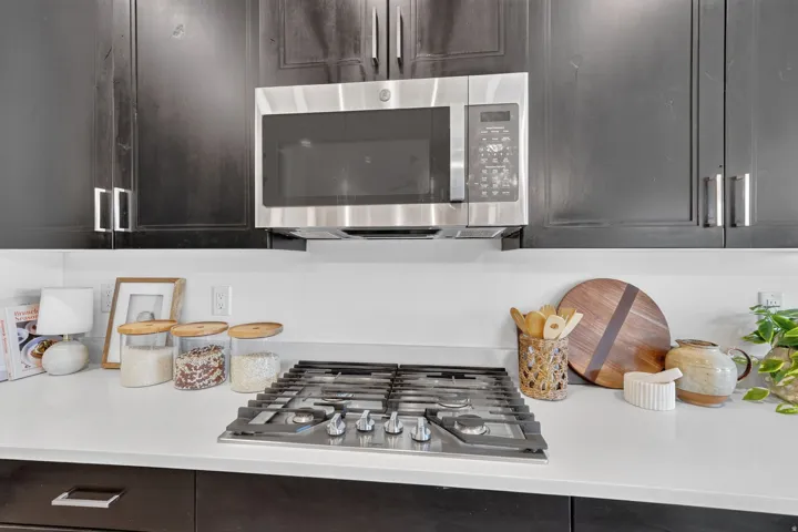 Built-in stainless steel microwave, gas cooktop, dark cabinetry, and light-toned countertops