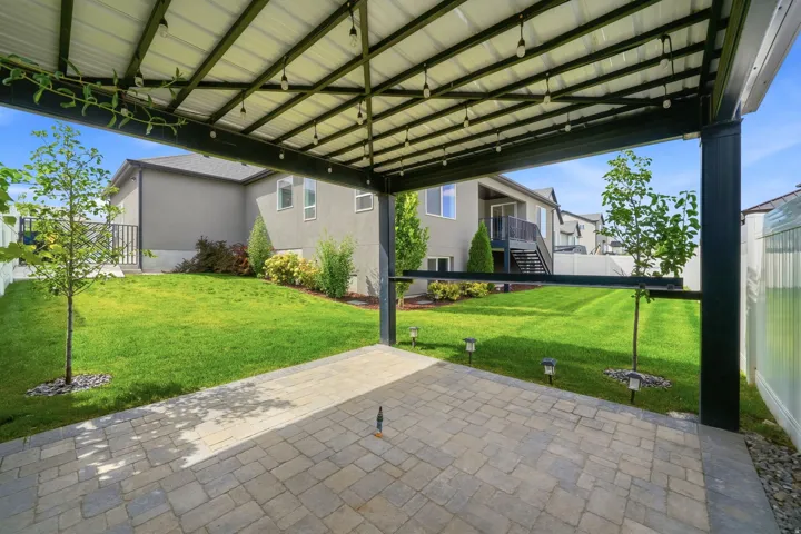 Covered patio with string lighting, paver stone surface, and a spacious green lawn