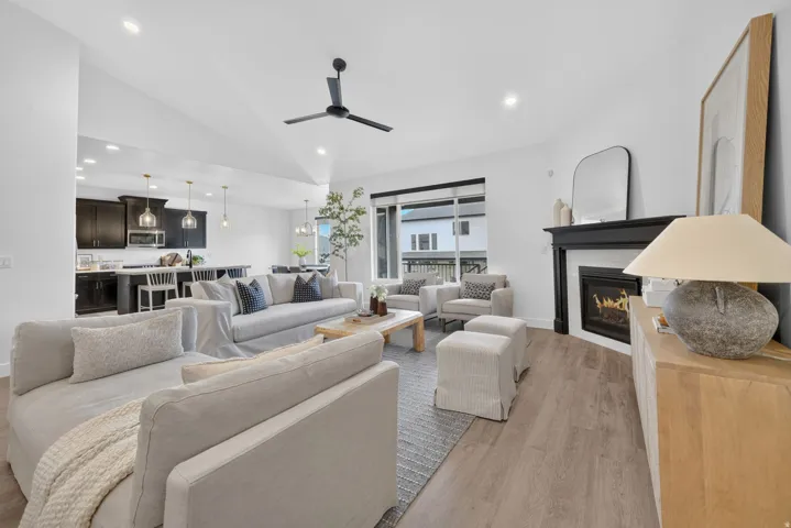 Open-concept living space featuring wood-finish flooring, a contemporary fireplace with a black mantel, recessed lighting, and a modern ceiling fan