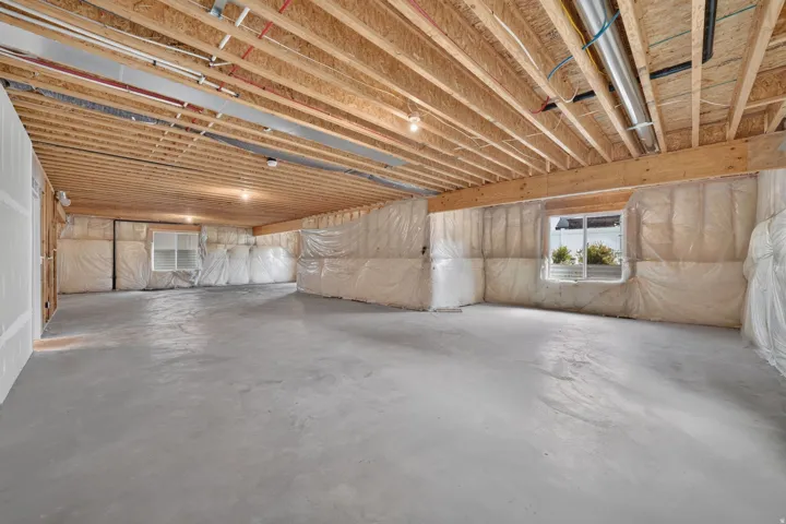 Expansive unfinished space featuring exposed ceiling joists, concrete flooring, and multiple windows