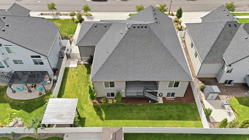 Expansive rear lawn, covered patio, white vinyl fencing, and a detached storage shed