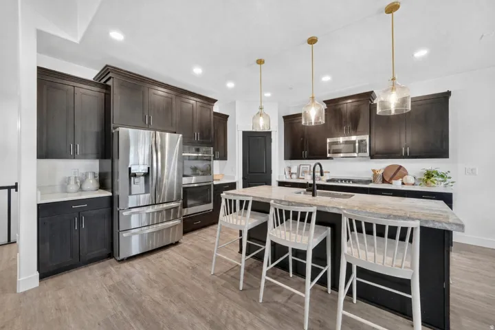Kitchen featuring dark wood cabinetry, stainless steel appliances, a large center island with counter seating, light-toned countertops, and wood-finish flooring