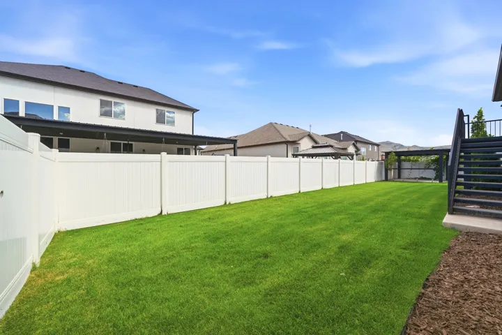 Expansive backyard featuring a manicured lawn, full privacy fencing, and an exterior staircase