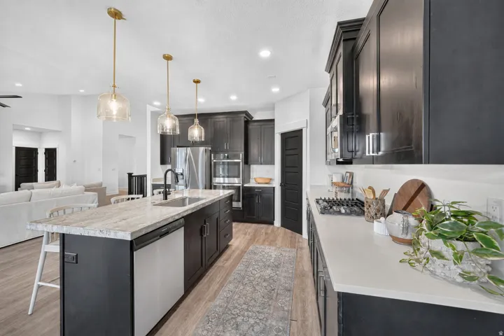 Kitchen featuring dark cabinetry, a center island with integrated sink, light-toned countertops, stainless steel appliances, and wood-finish flooring
