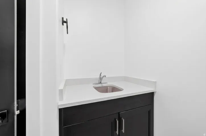 Built-in vanity with a stainless steel sink, solid surface countertop, and dark wood-finish cabinetry with silver hardware