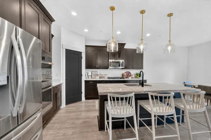 Kitchen featuring a large island with an undermount sink, dark wood cabinetry, stainless steel appliances, and wood-finish flooring