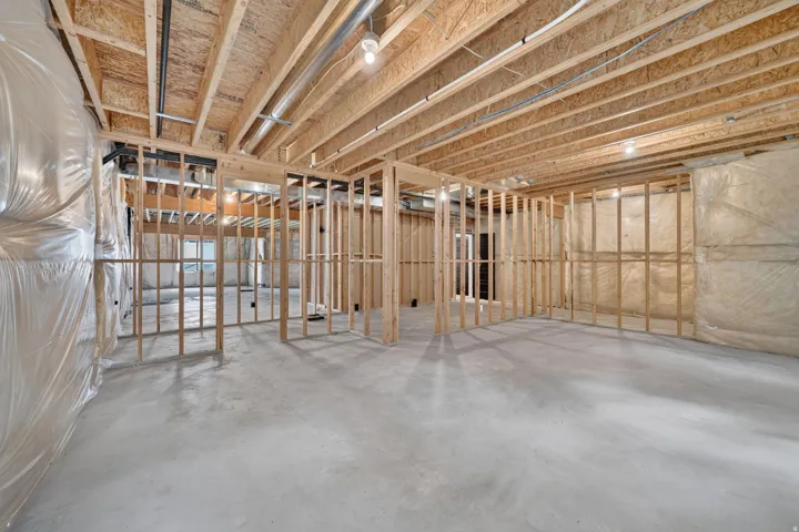 Unfinished basement with concrete flooring, exposed wooden joists, and framed partition walls