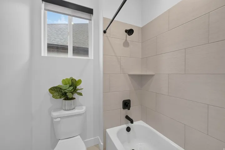 Bathtub with matte black fixtures, light-toned wall tile, and a built-in shower niche