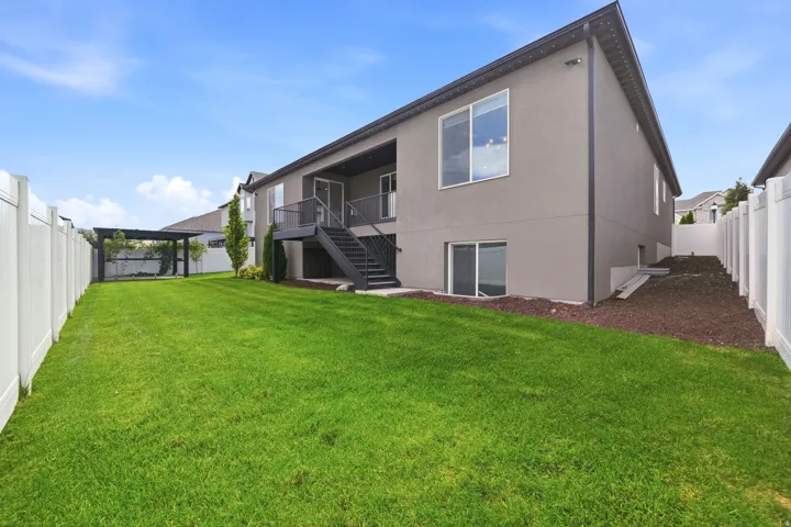 Expansive green lawn with a white privacy fence, a dark-toned pergola, and a multi-level deck with stairs