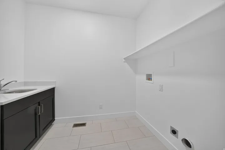 Laundry room featuring a utility sink, dark wood cabinetry, white countertop, and tile flooring