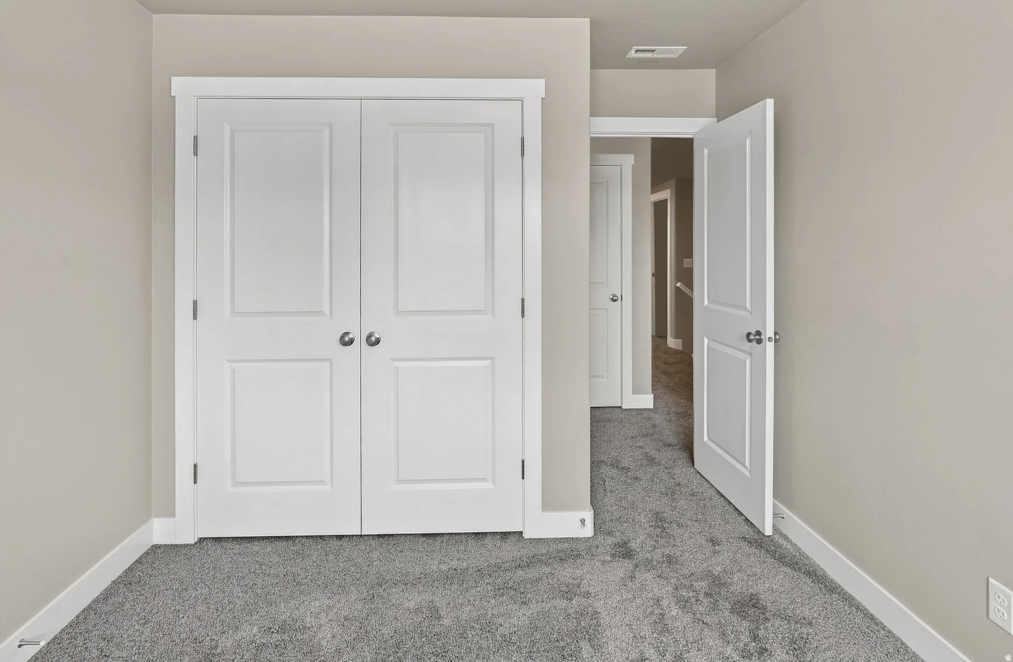 White paneled bifold closet doors, light gray wall paint, white trim, and gray carpeted flooring