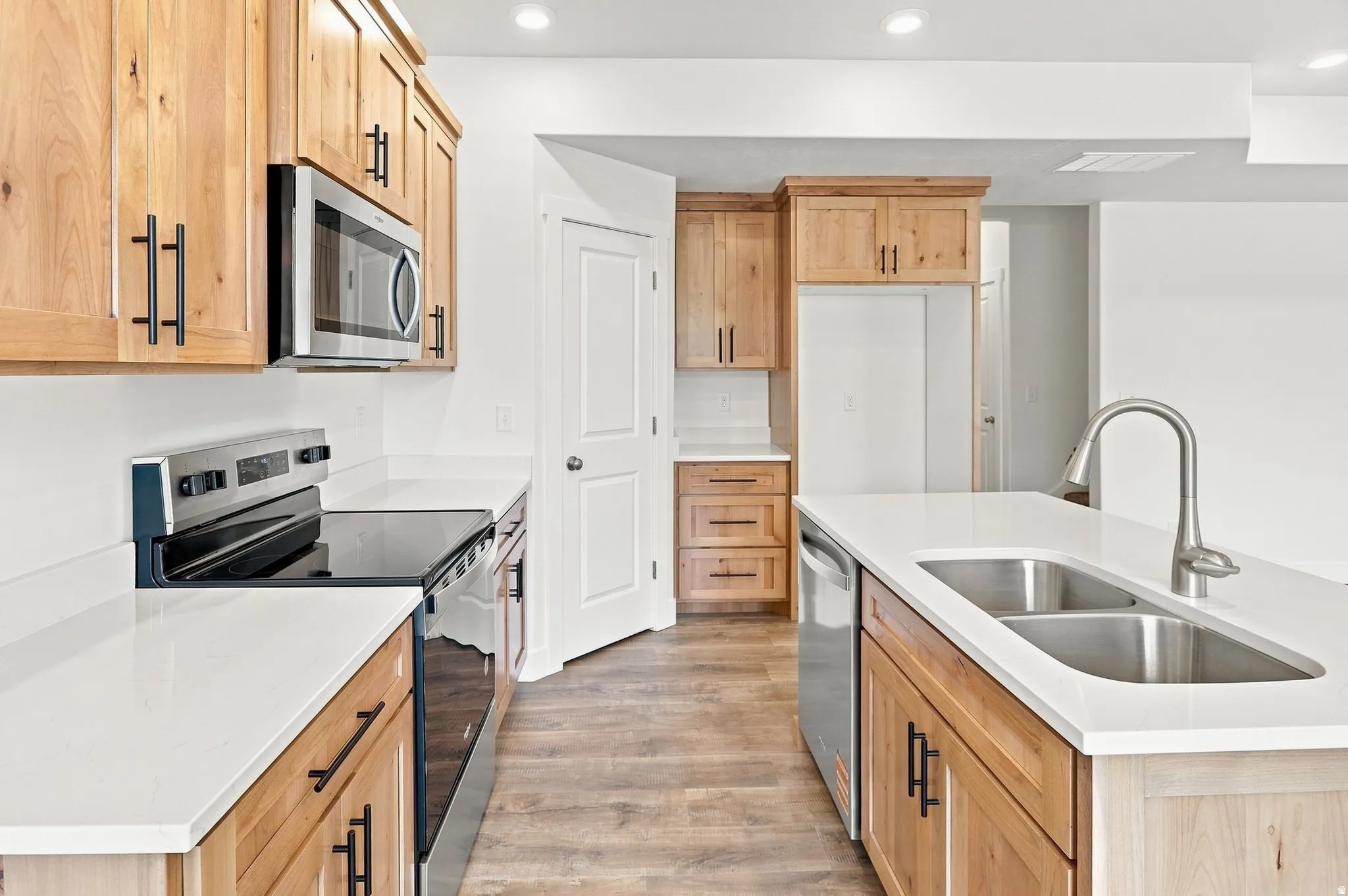 Light wood-finish cabinetry, stainless steel appliances, white countertops, and wood-finish flooring