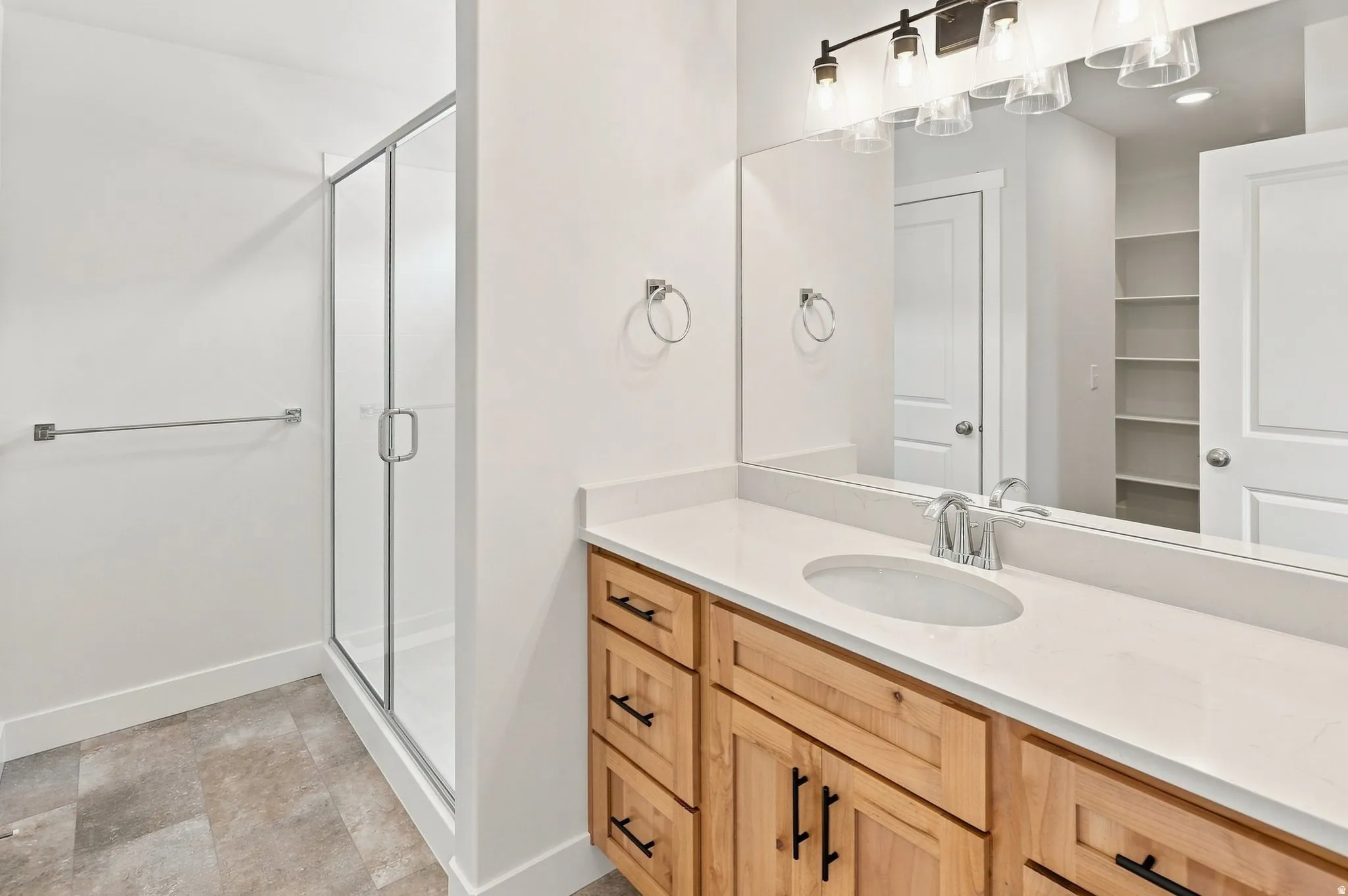 Walk-in shower with clear glass enclosure, single vanity with light wood cabinetry, white countertop, and contemporary black-finish vanity lighting