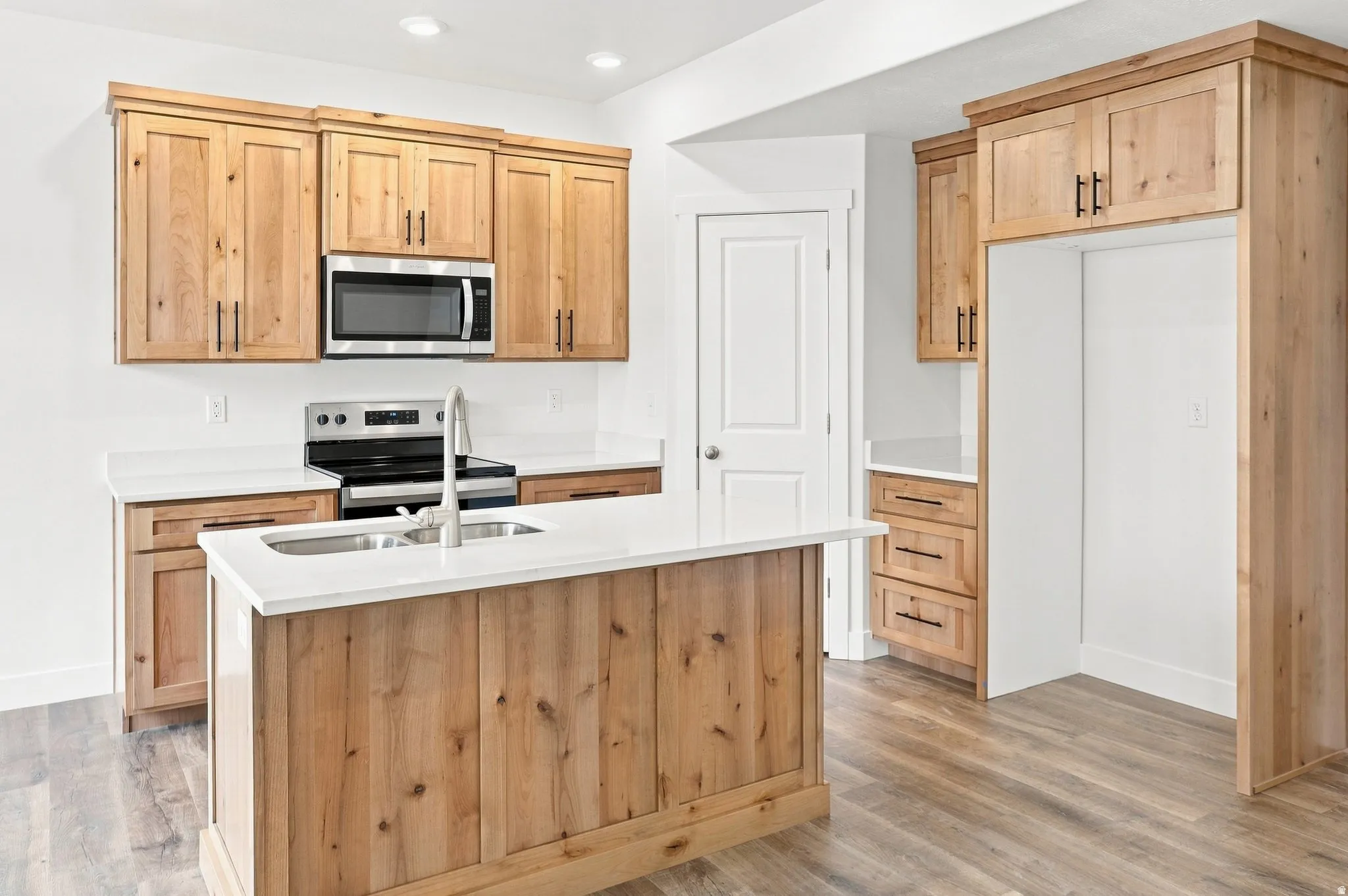 Kitchen featuring natural wood-finish cabinetry, stainless steel microwave, white countertops, and a central island with an integrated sink