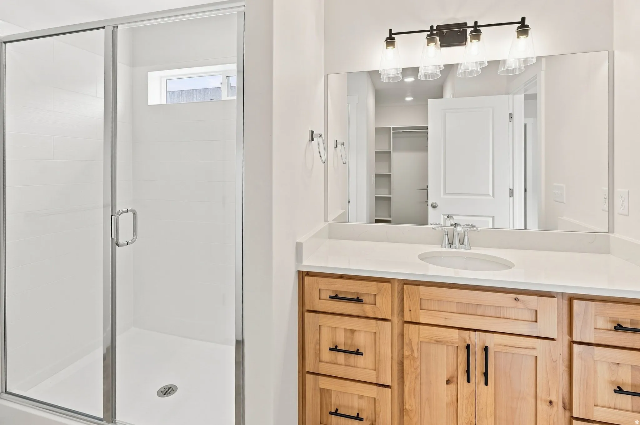 Frosted glass shower enclosure with a transom window, wood-finish vanity with ample storage, integrated basin, stone-finish countertop, and a four-bulb vanity light fixture