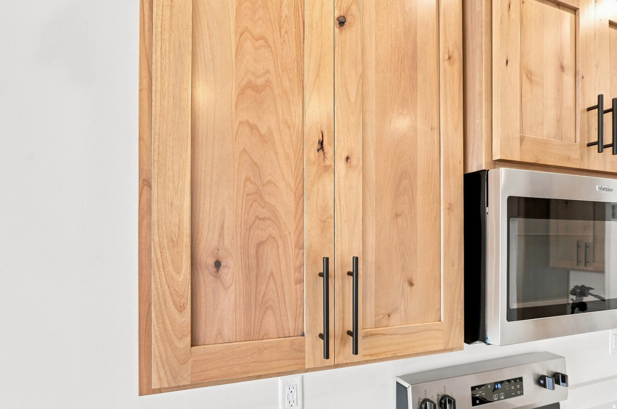 Natural wood-finish cabinetry with flat panel doors and matte black hardware, accompanied by stainless steel appliances