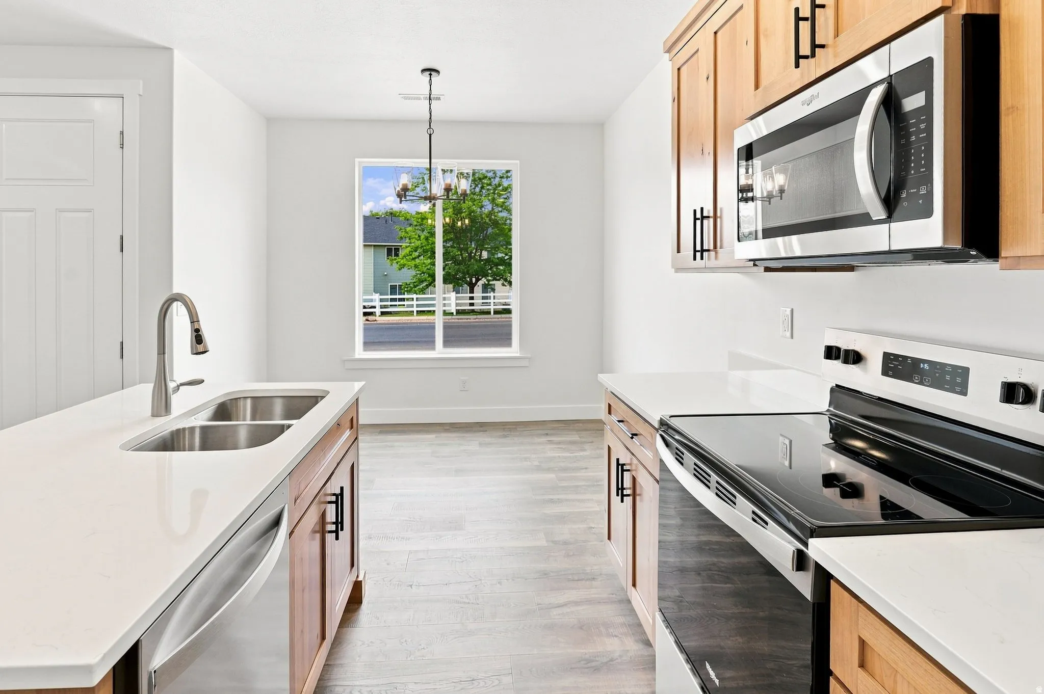 Kitchen featuring stainless steel appliances, light wood cabinetry, white countertops, and wood-finish flooring