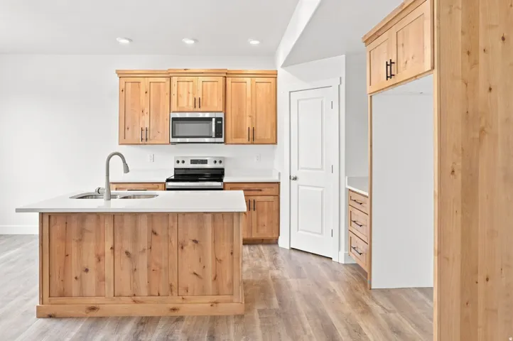 Kitchen featuring wood-finish cabinetry, stainless steel microwave, white countertops, and a center island with an undermount sink