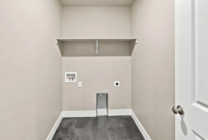 Utility space featuring a built-in shelf, dark stone-finish tile flooring, and a white paneled door with a brushed nickel knob