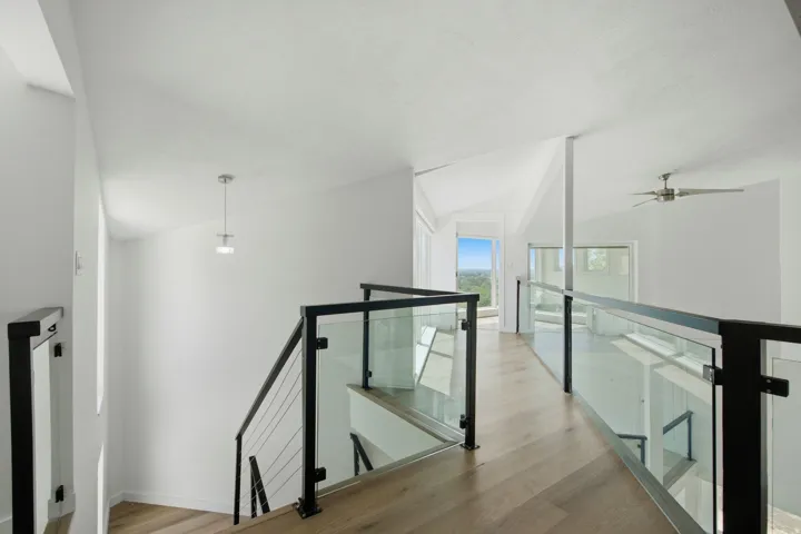High vaulted ceilings, wood-finish flooring, contemporary glass and metal railings, suspended light fixture, and a ceiling fan