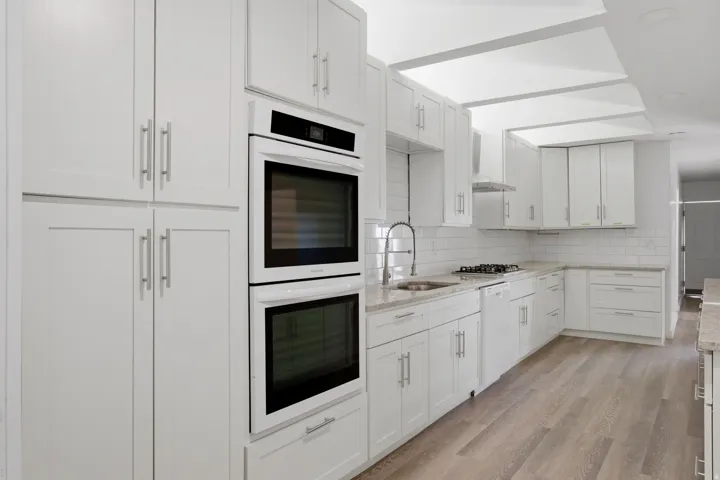 White shaker cabinetry, light-toned wood-finish flooring, white subway tile backsplash, light-toned countertops, and stainless steel appliances