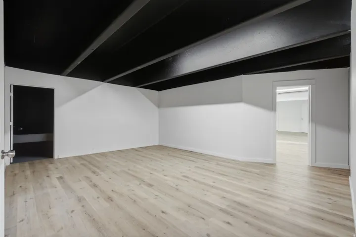 Expansive room with light wood-finish flooring, white walls, and an exposed black ceiling