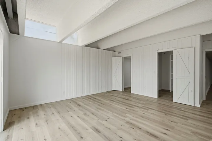 Wood-finish flooring, vaulted ceilings with exposed beams, transom windows, and white shiplap walls with barn-style doors